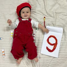 a baby laying on a bed next to some crayon markers and a drawing