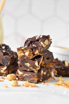 chocolate peanut butter fudge bars stacked on top of each other with nuts scattered around them