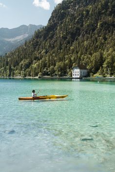 a person in a kayak paddling on the water with mountains in the background