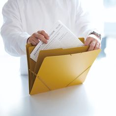 a man in white shirt holding an open envelope with papers inside it on top of a table