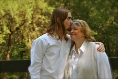 two people standing next to each other with trees in the background