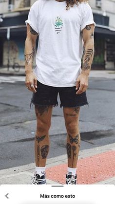 a man with long hair and tattoos standing on the side of the road wearing black shorts