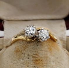 two diamond engagement rings sitting on top of a cushioned pillow in an old - fashioned box