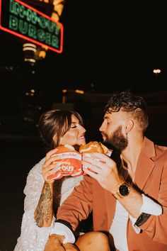 a man and woman sitting on the ground eating hotdogs in front of a basketball hoop