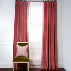 a chair sitting in front of a window next to a red drapeed curtain