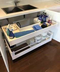 a kitchen sink under a counter with cleaning products and other items in the bottom drawer