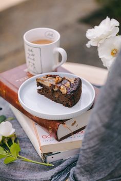 there is a piece of cake on a plate next to a book and cup of coffee