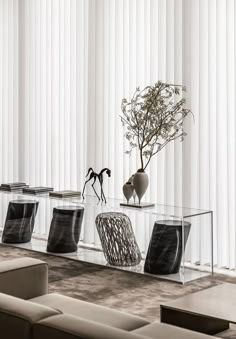 a glass coffee table with two vases and a plant on it in front of white vertical blinds