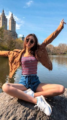 a woman sitting on top of a rock next to a lake with her arms in the air