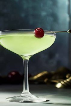 a green cocktail with a cherry on the rim