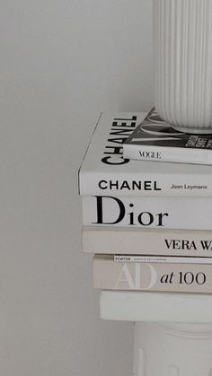 three books stacked on top of each other in front of a white vase and wall