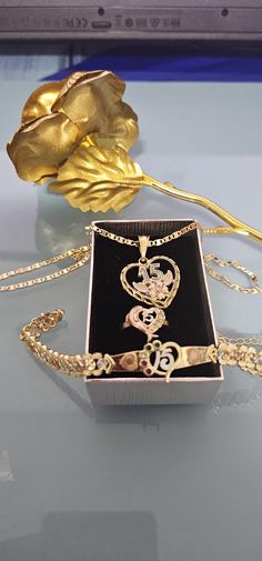 a box with a necklace on it sitting on a table next to a gold rose