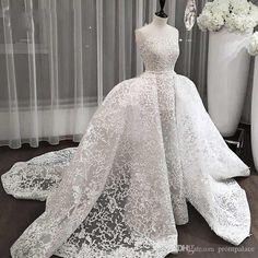 a white wedding dress on display in front of a window with flowers and curtains behind it