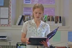 a woman standing in front of a desk holding a book