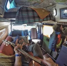 a man laying in the back of a van holding a guitar