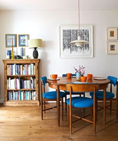 a dining room table with blue chairs and bookshelf in the backround