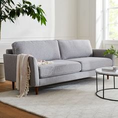 a grey couch sitting on top of a white rug in a living room next to a window