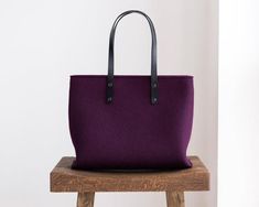 a purple tote bag sitting on top of a wooden stool next to a white wall