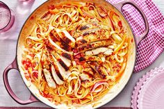 a pan filled with chicken and pasta on top of a table next to pink plates