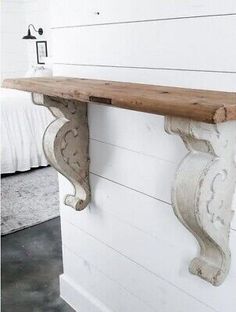 an old wooden shelf with decorative brackets on the top and bottom, against a white painted wall