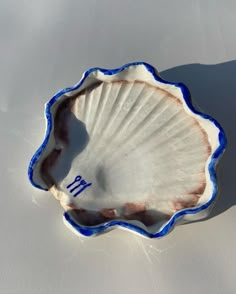 an empty shell shaped dish with blue trim on the bottom and writing in white ink