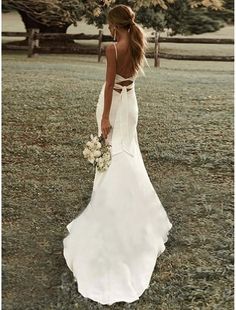 a woman in a white dress is standing in the grass with her back to the camera