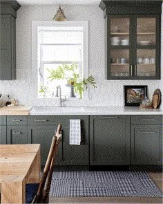 a kitchen with dark green cabinets and white tile backsplash, wooden dining table