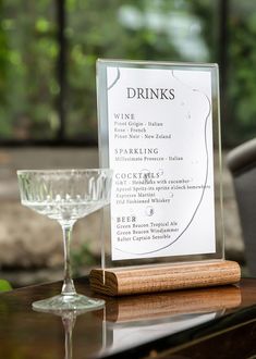 a wine glass sitting on top of a wooden table next to a sign that says drinks