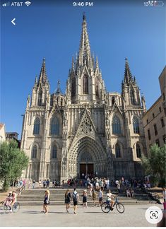 people walking and riding bikes in front of a large building with many spires on it