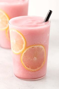 two glasses filled with pink smoothie topped with orange slices and a black straw on top