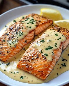 two salmon fillets on a white plate with lemon wedges