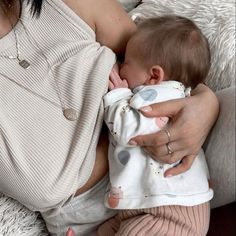 a woman holding a baby in her arms while laying on top of a white blanket