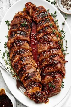 a white plate topped with meat covered in sauce and garnished with green herbs