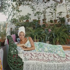 a woman laying on top of a bed next to potted plants