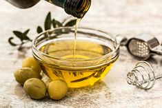 olives are being poured into a glass bowl with olive oil in it and an olive peeler next to the bowl