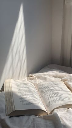 an open book sitting on top of a bed next to a white wall and window