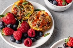 two white plates topped with muffins and berries next to another plate filled with fruit