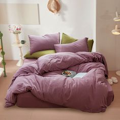 a bed with purple comforter and pillows in a white room next to a lamp