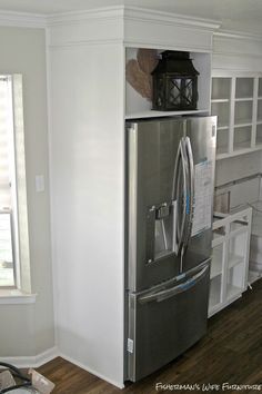 a stainless steel refrigerator in the corner of a kitchen with white cabinets and wood floors