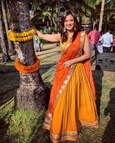 a woman standing next to a palm tree wearing an orange and yellow sari dress