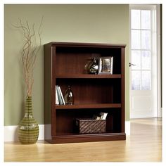 a wooden bookcase sitting on top of a hard wood floor next to a vase