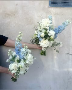 two women holding bouquets of white and blue flowers in their hands against a wall