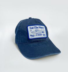 EAT THE WAVE - Yeah Sure Crafted with a classic silhouette and a faded blue hue. Hit the beach in ultimate comfort with our pre-washed cotton surf-style hat. Engineered to provide a relaxed, broken-in feel from the get-go. Adjustable Navy Baseball Cap For Beach, Navy Adjustable Baseball Cap For Summer, Vintage Sports Baseball Cap With Curved Bill, Vintage Curved Bill Baseball Cap For Sports, Vintage Curved Visor Summer Hat, Vintage Blue Baseball Cap For Sports, Vintage Adjustable Baseball Cap For Summer, Vintage Cotton Trucker Hat For Beach, Retro Dad Hat With Curved Bill For Summer