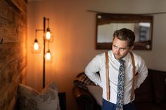 a man wearing suspenders and a tie standing in front of a couch with his hands on his hips