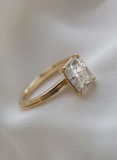 a gold ring with a princess cut diamond in the center on a white fabric background