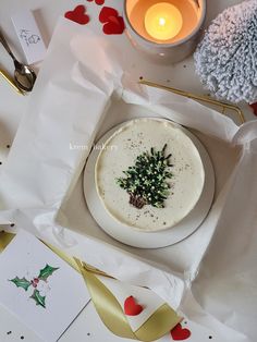 a white plate topped with a small green tree on top of a table next to a candle