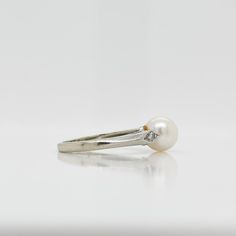 A fine Retro signed pearl cocktail ring.  In 14k white gold.  Set with 7mm round white pearl and flanked by two small accent diamonds on the shoulder of the setting.  Marked to the shank for Rothman & Schneider of New York City.  Simply a wonderful Mid-Century ring!  Date: Mid-20th Century  Overall Condition: It is in overall good, as-pictured, used estate condition with some fine & light surface scratches and other signs of expected light wear consistent with age.  Fineness: Marked 14k for gold White Pearl Ring With Diamond Accents And Akoya Pearl, Formal Pearl Drop Diamond Ring Fine Jewelry, Formal White Diamond Ring With Pearl Drop, Classic White Pearl Ring With Diamond Accents, Timeless White Gold Pearl Ring With Diamond Accents, Timeless White Round Cut Pearl Ring, White Timeless Round Cut Pearl Ring, White Akoya Pearl Rings With Diamond Accents, Classic White Gold Pearl Ring With Diamond Accents