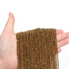 a hand is holding a piece of gold colored beaded fabric on a white background