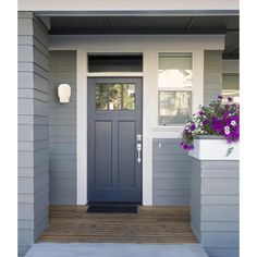 a blue front door on a gray house with purple flowers in the window box and white trim