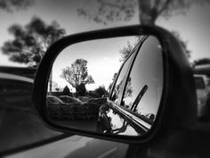 the rear view mirror on a car shows cars parked in a parking lot and trees